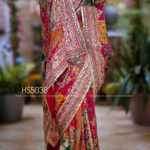 May include: A multi-colored crepe saree featuring intricate Aari hand embroidery, mirror work, and a wide decorative border. The fabric displays a vibrant pattern of pink, orange, and green. Text on the image reads HS5036 PURE CREPE SAREE.