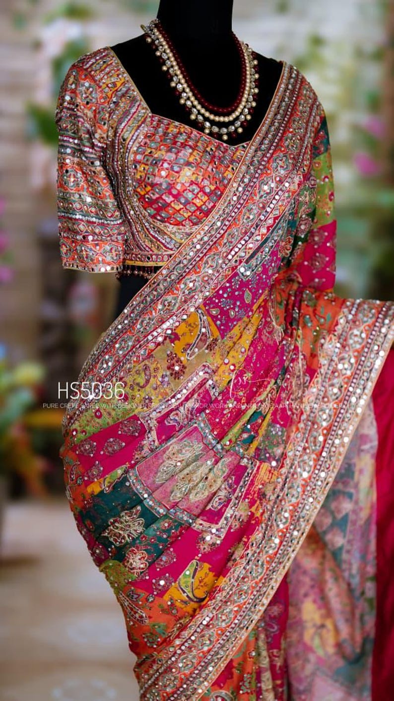 May include: A vibrant multi-colored saree featuring intricate embroidery, mirror work, and patchwork patterns in shades of pink, orange, and green. The garment includes a matching blouse with detailed mirror embellishments and the text HS5036.
