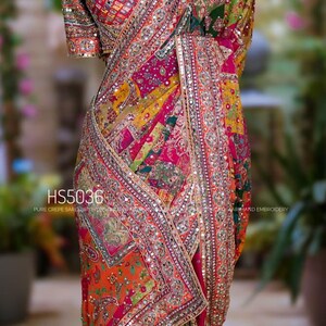 May include: A multi-colored crepe saree featuring intricate embroidery, mirror work, and a patchwork design in shades of pink, orange, green, and yellow. The garment includes a matching blouse and is labeled with the text HS5036.