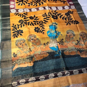May include: A decorative textile featuring a vibrant yellow background with black floral patterns and a border. The design includes figures in orange and blue, with a central blue figure playing a flute. The textile has a dark green border.