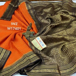 May include: An orange and gold saree with intricate patterns and a decorative border. The saree features the text "IWZ W17401" and is draped, showcasing its texture and design. A small decorative item and a tag are also visible.