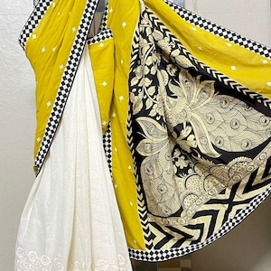 May include: A vibrant saree featuring a white, yellow, and black color scheme. The saree showcases a white embroidered border, a yellow body, and a black patterned border. The design includes a black and white checkered pattern and a detailed peacock motif.