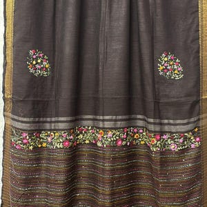 May include: Dark brown textile with embroidered floral patterns in pink, yellow, and green. The fabric has a striped design at the bottom and a gold border. The floral embroidery is scattered across the textile.