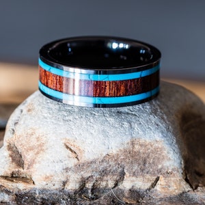 May include: A black tungsten carbide ring with a brown wood inlay and a turquoise blue accent.