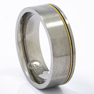 May include: A silver wedding band with a thin gold band around the edge.