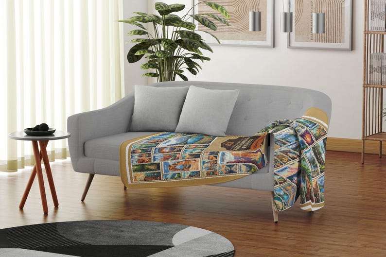 May include: A gray couch with two pillows and a throw blanket with a colorful pattern of national park stamps. The blanket is draped over the back of the couch and hangs down the side.