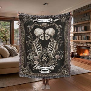 May include: A black and white woven tapestry with a gothic design featuring two skeletons holding hands and kissing. The tapestry has a floral border and the text "Thick as Thieves Est. 2023" at the bottom.