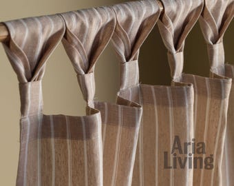 May include: Beige and white striped curtains hanging from a wooden rod. The curtains have a textured appearance and are gathered at the top, creating a decorative effect. The text "Aria Living" is visible on the curtain.