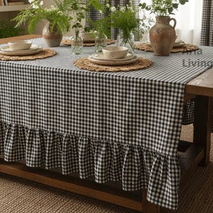 Puede incluir: Una mesa de comedor preparada para una comida, con un mantel a cuadros blanco y negro con un borde con volantes. La mesa está puesta con platos, manteles individuales tejidos y jarrones con vegetación. La habitación tiene cortinas a cuadros a juego.