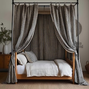 Puede incluir: Una cama con dosel de madera con una cortina a cuadros en blanco y negro. La cama está hecha con sábanas y almohadas blancas. El marco de la cama es de color marrón claro. La habitación tiene una paleta de colores neutros con una alfombra tejida.