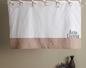May include: A white and tan valance with brown ties hanging from a wooden rod. The bottom of the valance is tan, and the text "Aria Living" is printed in gray on the right side. The valance is made of fabric.