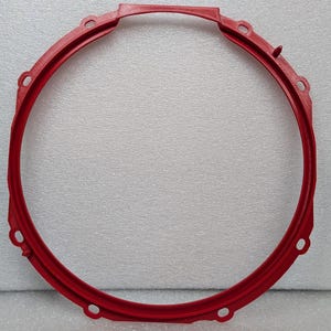 May include: A bright red, circular object with a handle and several evenly spaced holes. The object appears to be made of a solid material and has a smooth, matte finish. The design suggests a mechanical or industrial component.