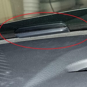 Op de afbeelding: Een zwart, rechthoekig object is gemonteerd op het dashboard van een voertuig, in de buurt van de voorruit. Het object lijkt gemaakt te zijn van een glad, donker materiaal en is horizontaal geplaatst. Het dashboard is donkergrijs.