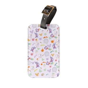 May include: A rectangular luggage tag with a black leather strap and gold buckle. The tag features a white background with a colorful pattern of cartoon characters, paint splatters, and the word "Epcot".