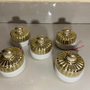 May include: Five gold and white ceramic light switch covers with a decorative, fluted design.