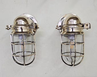 May include: Two polished chrome nautical bulkhead lights with clear glass cage covers and a caged light bulb inside each.