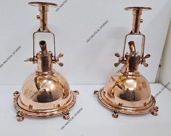 May include: Two polished copper nautical bulkhead lights with adjustable arms and a dome-shaped shade. Each light has a decorative ring around the base and three feet.