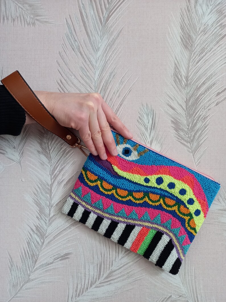 May include: A colourful beaded clutch with a pink lining and a brown strap. The clutch features a geometric design with a wavy pattern and a large eye in the centre.