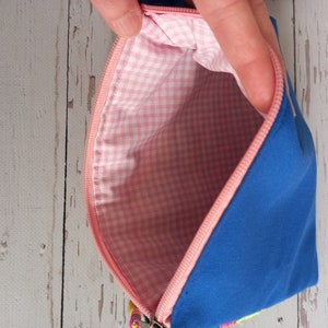 May include: A blue zippered pouch with a pink and white gingham lining. The pouch is open and the lining is visible.