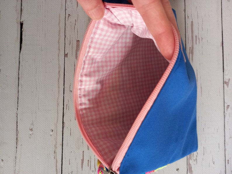 May include: A blue zippered pouch with a pink and white gingham lining. The pouch is open and the lining is visible.