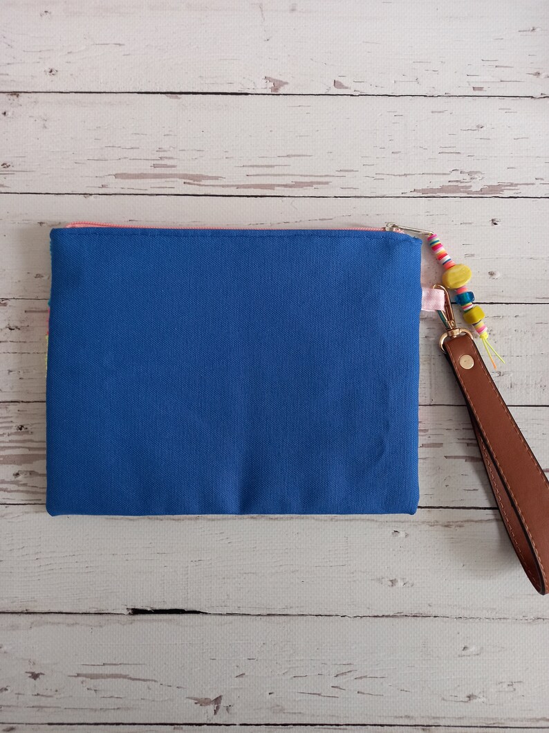May include: A blue canvas zippered pouch with a pink zipper and a brown leather strap with colourful beads.