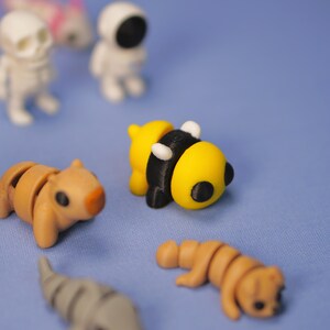 Op de afbeelding: Een verzameling kleine, kleurrijke, 3D-geprinte figuurtjes, waaronder een bij, een beer, een skelet en een astronaut. De figuurtjes staan op een blauwe ondergrond.