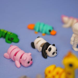 Op de afbeelding: Een verzameling kleine, kleurrijke, 3D-geprinte dierenfiguren. De figuren zijn gemaakt van plastic en zijn ontworpen om te worden gearticuleerd. De dieren omvatten een panda, een varken, een vogelbekdier, een krokodil en een giraffe.