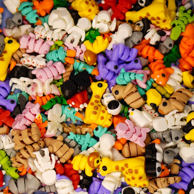 Op de afbeelding: Een grote verzameling kleurrijke, kleine, plastic figuurtjes van verschillende dieren, waaronder giraffen, vlinders en lieveheersbeestjes. De figuurtjes zijn in een willekeurig patroon gerangschikt en zijn allemaal van verschillende grootte.