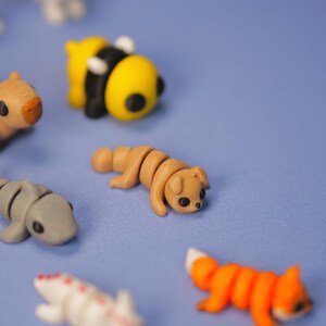 Op de afbeelding: Een verzameling kleine, kleurrijke dierenfiguren gemaakt van polymer clay. De figuren omvatten een ​​bij, een hond, een vos, een haai en een capibara.