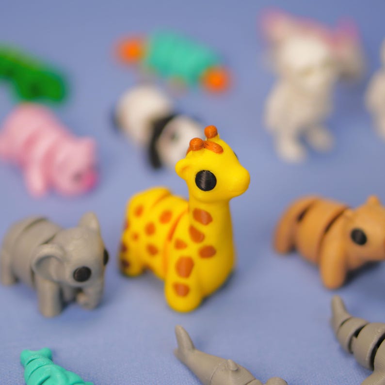 Op de afbeelding: Een verzameling kleine, kleurrijke dierenfiguren, waaronder een giraffe, een olifant, een varken, een panda en een haai. De figuren zijn gemaakt van plastic en hebben een cartoonachtige stijl.