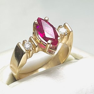 May include: A gold ring with a marquise-shaped ruby gemstone and two smaller diamond accents.