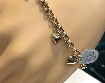 Op de afbeelding: Een gouden kettingarmband met meerdere hartcharms. De armband zit om de pols van een model.