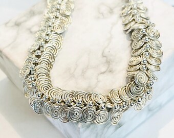May include: A silver necklace made of coiled wire and small beads. The necklace is arranged in a wave-like pattern.