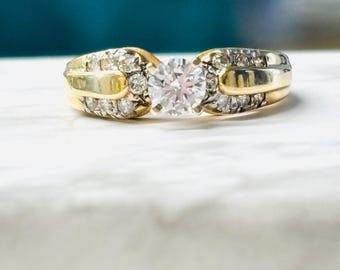 May include: A gold engagement ring with a round, clear diamond center stone and smaller diamonds set in the band.