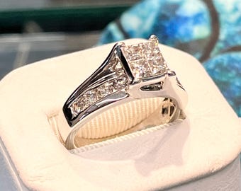 May include: A silver engagement ring with a square-cut diamond center stone and smaller diamonds on the band. The ring is set on a white surface, showcasing its brilliance. A classic and elegant piece of jewelry.