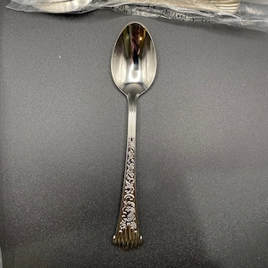 以下が含まれることがあります： ハンドルに装飾的な花柄が施された銀製のティースプーン。スプーンは磨かれて光沢があります。