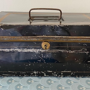 May include: A black metal vintage tin box with a brass latch and a gold trim. The box has a worn, distressed look.