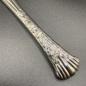 Puede incluir: Un cuchillo de plata con un diseño floral ornamentado en el mango. El mango es redondeado y tiene un patrón acanalado.