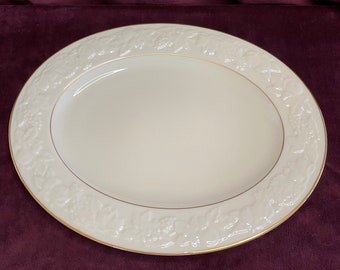 Könnte beinhalten: Eine weiße ovale Servierplatte mit einem erhabenen Blumendesign am Rand. Die Platte hat einen goldenen Rand.