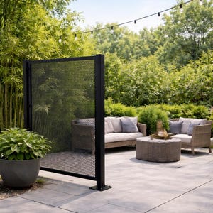 Peut inclure: Un écran de confidentialité en métal noir doté d'un motif de grille perforée avec de petits trous circulaires, soutenu par un cadre vertical robuste, placé sur une terrasse en pierre à côté d'une grande plante en pot et d'un salon de jardin.