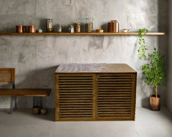 Könnte beinhalten: Ein Holzschränkchen mit Lamellentüren steht vor einer Betonwand. Der Schrank hat eine hellbraune Oberfläche und steht auf einem weißen Fliesenboden. Rechts neben dem Schrank steht eine kleine Topfpflanze auf dem Boden.