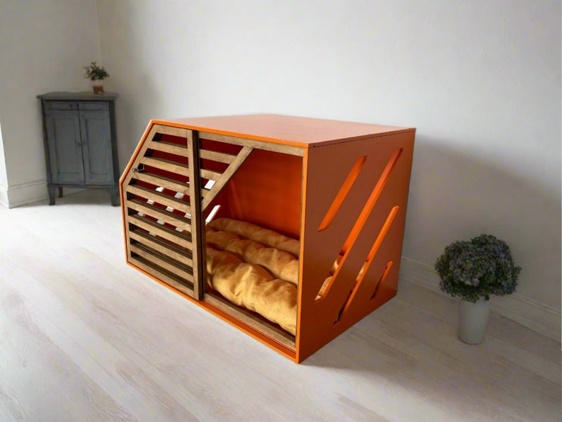 May include: Orange wooden dog crate with a slatted door and a brown cushion inside. The crate has a modern design with diagonal cutouts on the front.