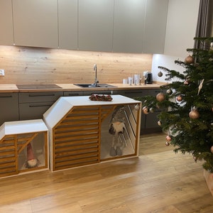 May include: Two white wooden storage units with slatted wooden fronts and a gnome figurine inside each. The units are in a kitchen with a wood countertop and a Christmas tree in the background.