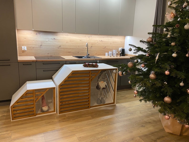 May include: Two white wooden storage units with slatted wooden fronts and a gnome figurine inside each. The units are in a kitchen with a wood countertop and a Christmas tree in the background.