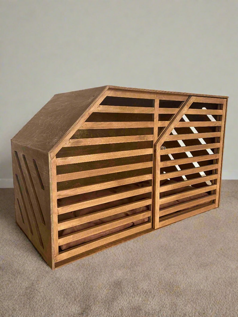May include: A wooden dog crate with a slatted front and a solid side panel. The crate has a brown stain and a brown cushion inside.