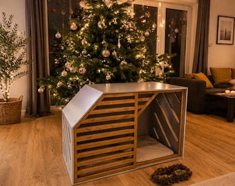 Op de afbeelding: Een rechthoekige dierenbench met een lichtgrijs frame en horizontale houten latten aan het voorpaneel. De structuur heeft een schuine bovenkant en een open zijkant met diagonale houten latten. Binnenin ligt een lichtgekleurd kussen.