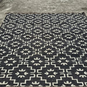 May include: A black and white geometric patterned rug. The rug features a repeating pattern of white shapes on a black background. The rug has a fringed edge.