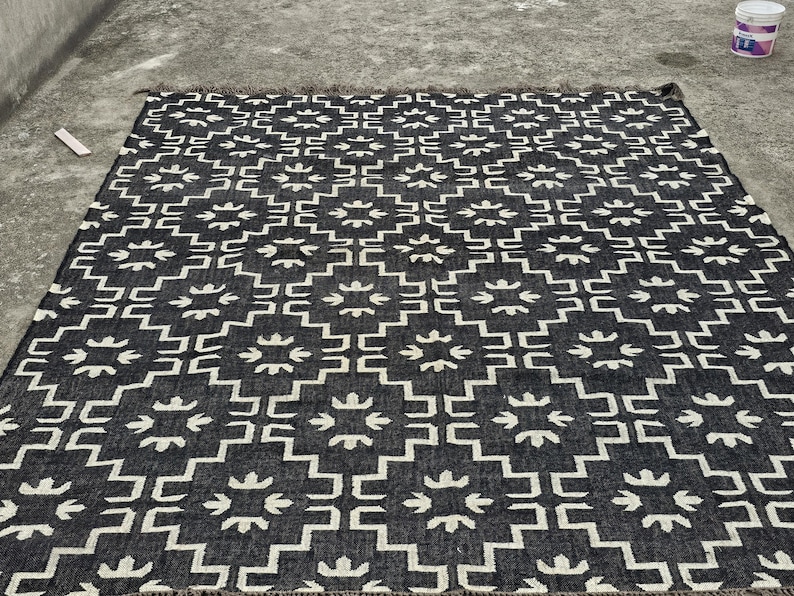 May include: A black and white geometric patterned rug. The rug features a repeating pattern of white shapes on a black background. The rug has a fringed edge.