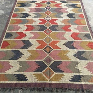 May include: A large, rectangular rug with a geometric pattern in shades of brown, red, pink, and gray. The rug has a fringe border.