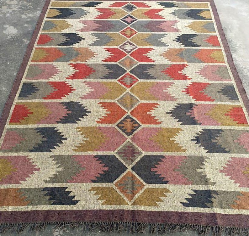 May include: A large, rectangular rug with a geometric pattern in shades of brown, red, pink, and gray. The rug has a fringe border.